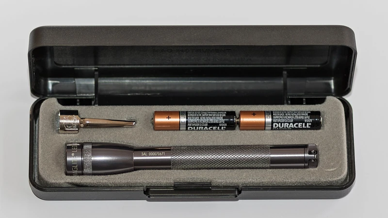 Mini Maglite LED 2-cell AA flashlight (gray finish shown) in its open black presentation case next to two AA batteries.