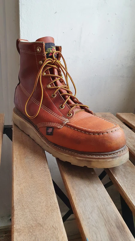 Thorogood American Heritage 6-inch moc toe work boot (804-4200) in tobacco leather with a cream wedge sole, on a wooden bench.