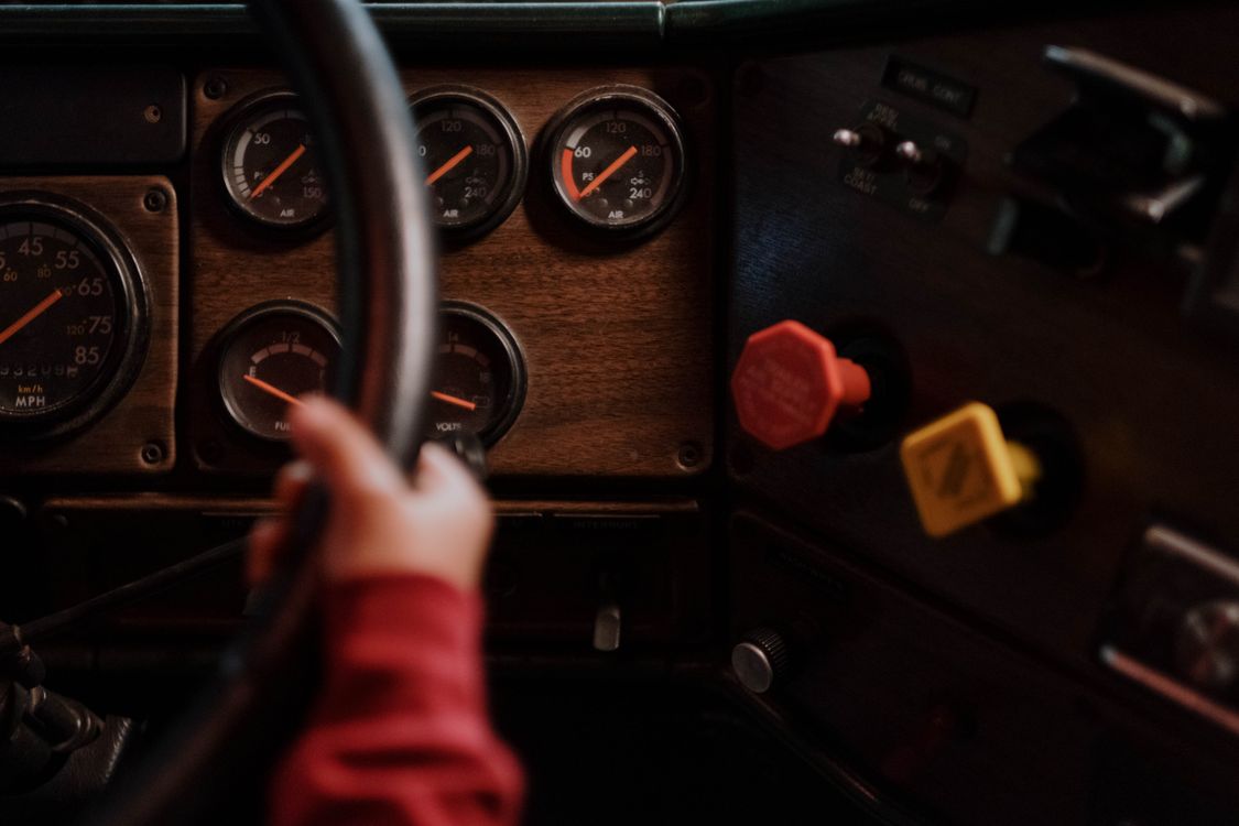 Close-up of a semi truck dashboard: gauges, air pressure dials, and the red and yellow air brake knobs.