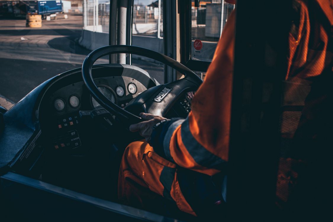Driver in a high-visibility jacket with hands on the steering wheel inside a semi truck cab.
