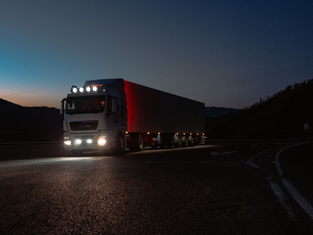 Semi truck with headlights on driving at dusk.